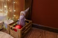 Christmas toy, Santa Claus or festive gnome in hat in wooden box with red bauble for fir-tree. Shiny garland lights, copy space. Royalty Free Stock Photo