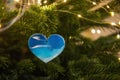 Christmas toy in the shape of a heart with the image of waves of the blue sea hangs on a green tree Royalty Free Stock Photo