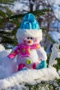 Christmas toy snowman in a blue cap sitting on the snow on the branches of the Christmas tree close up. Royalty Free Stock Photo