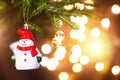 Christmas toy Snowman in a red hat with a scarf on live branch of a fir tree with Golden lights of garlands in defocus. New year, Royalty Free Stock Photo