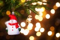 Christmas toy Snowman in a red hat with a scarf on live branch of a fir tree with Golden lights of garlands in defocus. New year, Royalty Free Stock Photo