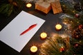 Christmas toys, burning candles and notebook lying near green spruce branch on black background top view. Space for text Royalty Free Stock Photo