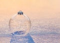 Christmas transparent bauble ornament covered with sparkling shiny snowflakes at sunset light on snow surface.