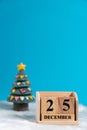 Christmas tree backside wooden block calendar set on the Christmas date 25 december on white wool and blue background. Copy space