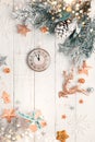 Christmas tree branch with pine cone in snow and retro style clock on a white wooden background. Winter or Christmas festive Royalty Free Stock Photo