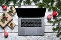 Christmas tree branches and gift boxes on rough white planks with opened laptop with blank screen