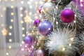 Christmas tree branches with purple decorative bulbs and warm lights bokeh. Shiny sparkling garlands. New Year eve