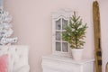 A Christmas tree in a ceramic pot stands on a white dresser in the living room, decorated for Christmas or New Year. Retro wooden