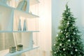 Christmas tree in the corner of the room next to a white rack with shelves. Modern decor in the house for the holiday. Abstract ba