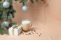 Christmas tree, decorated with balls, a gift box, a mug with coffee and milk on the background of flesh-colored waves Royalty Free Stock Photo