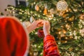 Christmas tree Decorating. Girl child in santa hat decorate the Christmas tree with red shiny balls.hands put red balls Royalty Free Stock Photo