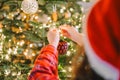 Christmas tree Decorating. Girl in santa hat and plaid pajamas decorate the Christmas tree with red shiny balls.hands Royalty Free Stock Photo