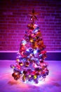 Christmas tree with festive lights in snow outdoors, purple brick wall background Royalty Free Stock Photo