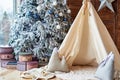 Christmas tree with gifts and wigwam near window in child room, copy space. Christmas decorations. Childen room interior.