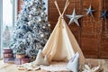 Christmas tree with gifts and wigwam near window in child room, copy space. Christmas decorations. Childen room interior.