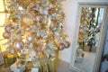 A Christmas tree with a Golden decoration is reflected in the mirror. New year, home decoration. Large window with yellow warm lig