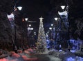 Christmas tree in lights and snow in park alley with street lamps at night Royalty Free Stock Photo