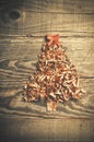 Simple Christmas tree arranged from sawdust, wood-chips on wooden background. Orange cute ribbon.