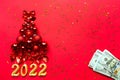 Christmas tree made of glass balls on a red background with gold sequins and 2022 and stack of $100. Christmas decor of finance, Royalty Free Stock Photo