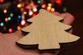 Christmas tree made of handmade wood in a female hand against the background of a Christmas garland. Concept of Royalty Free Stock Photo