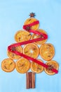 Christmas tree made from orange candied slices, cinnamon sticks, anise stars, and cloves, decorated with red ribbon, on  a blue Royalty Free Stock Photo