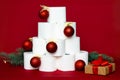 Christmas tree made from rolls of toilet paper, decorated with shiny balls, a gift and fir branches on a red background