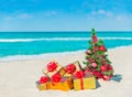 Christmas tree with red balls and golden fancy gift boxes at tropical sandy beach against ocean. New Year greeting card with Royalty Free Stock Photo