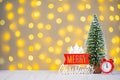 Christmas tree, red clock and wooden lettering Merry Christmas on light bokeh background.