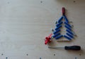 Christmas tree shape with dowels, nuts, screws, screwdriver and gift on a plywood background. Cope space, top view