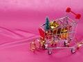 Christmas tree in shopping cart on background of shiny pink satin as background, silk background, Christmas card. Happy Royalty Free Stock Photo