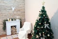 Christmas tree stands near the bedside table and fireplace against the white wall. Theme happy new year. Paper deer head hanging o Royalty Free Stock Photo