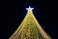 Christmas tree with yellow garlands, decorative bulbs and big white star topper at night blue sky