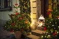 Christmas trees decorated with garland lightings and bowknots of red ribbon, vintage lantern outdoors on doorsteps in european old Royalty Free Stock Photo