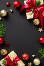 Christmas vertical banner. Frame made of gift boxes with red ribbon bow, fir branches, gold and red baubles on black background. Royalty Free Stock Photo