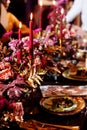 Christmas wedding dinner served table. Shiny leaves of gold paint, pink and red flowers and gold dishes. candles in a metal Royalty Free Stock Photo