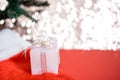 Christmas white gift box with a large bow standing on red hat santa calus against a background bokeh of twinkling golden bokeh