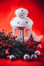 Christmas white lantern is standing with a burning candle in it with a fir tree branch and knit stars on a red background. Royalty Free Stock Photo