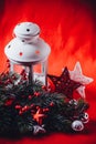 Christmas white lantern is standing with a burning candle in it with a fir tree branch and knit stars on a red background. Royalty Free Stock Photo