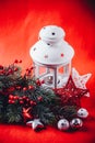 Christmas white lantern is standing with a burning candle in it with a fir tree branch and knit stars on a red background. Royalty Free Stock Photo