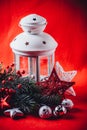 Christmas white lantern is standing with a burning candle in it with a fir tree branch and knit stars on a red background. Royalty Free Stock Photo