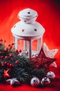 Christmas white lantern is standing with a burning candle in it with a fir tree branch and knit stars on a red background. Royalty Free Stock Photo