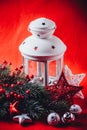 Christmas white lantern is standing with a burning candle in it with a fir tree branch and knit stars on a red background. Royalty Free Stock Photo