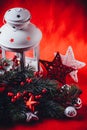 Christmas white lantern is standing with a burning candle in it with a fir tree branch and knit stars on a red background. Royalty Free Stock Photo