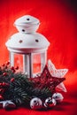 Christmas white lantern is standing with a burning candle in it with a fir tree branch and knit stars on a red background. Royalty Free Stock Photo