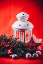 Christmas white lantern is standing with a burning candle in it with a fir tree branch and knit stars on a red background. Royalty Free Stock Photo