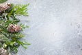 Christmas or winter background with a border of green and frosted evergreen branches and pine cones on a grey vintage board. Flat