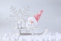 Christmas or winter composition. Young snowman with red woolen cap laying and sleeping on white wooden sledge. Royalty Free Stock Photo