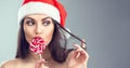 Christmas woman. Beauty model girl in Santa Claus hat eating red xmas lollipop candy Royalty Free Stock Photo