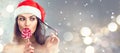 Christmas woman. Beauty model girl in Santa Claus hat with red lips and xmas lollipop candy. Closeup portrait