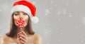 Christmas woman. Beauty model girl in Santa Claus hat with red xmas lollipop candy, gift. Sales. Surprised expression